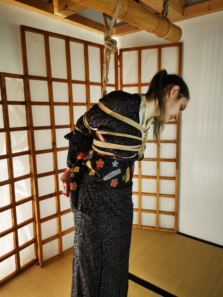 Foto di Shibari, con Kiki in elegante Kimono nero, legata e sospesa da Davide La Greca "MaestroBD" presso Koguma Dojo a Spazio Musubi