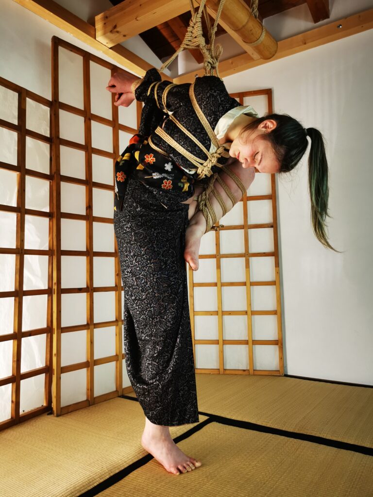Foto di Shibari, con Kiki in elegante Kimono nero, legata e sospesa da Davide La Greca "MaestroBD" presso Koguma Dojo a Spazio Musubi